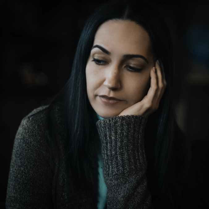 selective focus portrait photo of sad woman in gray sweater with her hand on her cheek
