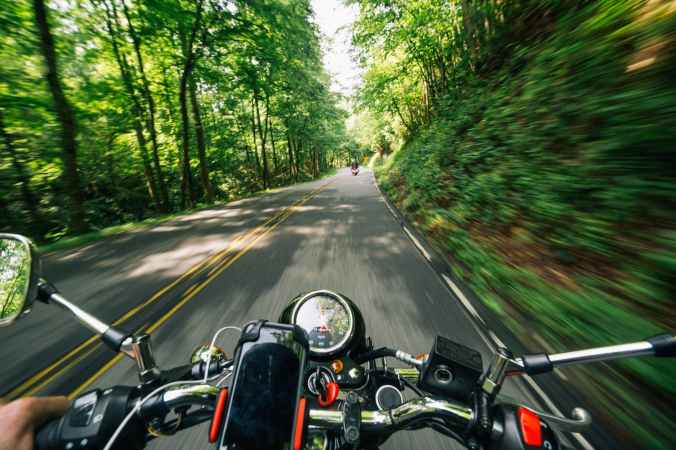 photo of person riding motorcycle on road between trees